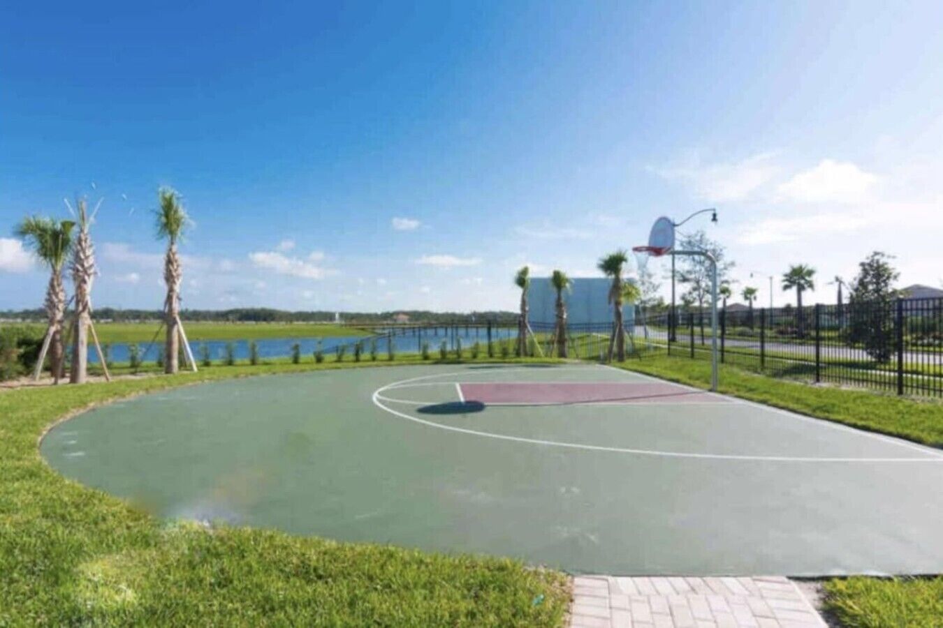 Un terrain de basketball en plein air offrant une vue dégagée sur le paysage environnant, notamment sur une étendue d’eau et une clôture.
