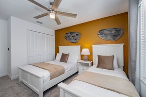 A bedroom with two beds, a ceiling fan, a nightstand with a lamp, and a door.