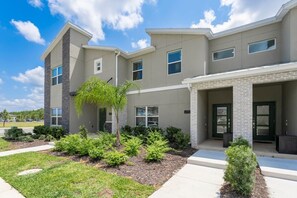 A modern multi-story building with a landscaped front yard, including a small palm tree and shrubs.