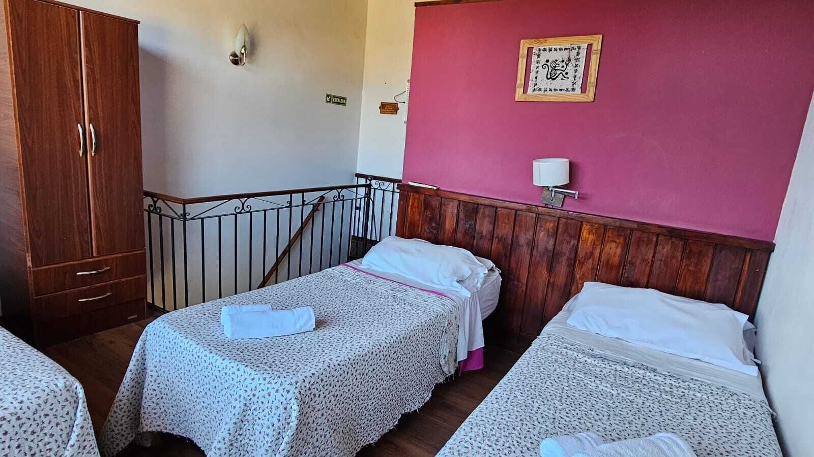 A room with two single beds, a wooden wardrobe, a staircase, and a wall with a framed picture.