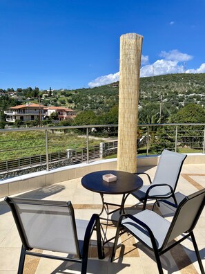 A terrace with a table and chairs, a bamboo pillar, and a view of a hillside with houses. - Villa Eva in Eretria Greece , the ideal place for your vacations (Eretria)