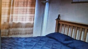 A room with a bed, a wooden headboard, a window with curtains, and a wall-mounted lamp. - Impeccable 1-bed Apartment in Purfleet (Purfleet)