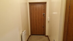 A narrow hallway with a wooden door at the end, a white radiator on the left, and a white wall. - Impeccable 1-bed Apartment in Purfleet (Purfleet)