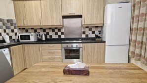 A kitchen with wooden cabinets, a microwave, a stove, and a refrigerator. - Impeccable 1-bed Apartment in Purfleet (Purfleet)
