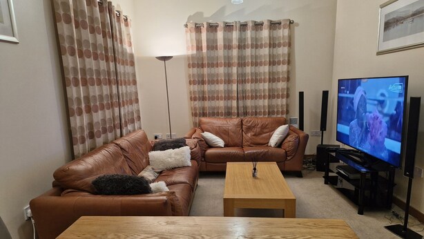 A living room with two brown leather sofas, a wooden coffee table, and a flat-screen TV on a stand. - Impeccable 1-bed Apartment in Purfleet (Purfleet)