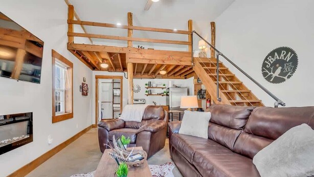 Ein geräumiges Wohnzimmer mit hohen Decken, freiliegenden Holzbalken, einem braunen Ledersofa, einem Couchtisch mit Dekoration und einer Treppe, die zu einer oberen Ebene führt.