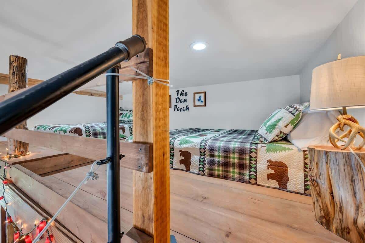 A cozy cabin-style room with a bed featuring a forest-themed bedding, a wooden headboard, and a wall-mounted lamp.