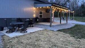 Ein Terrassenbereich im Freien mit überdachter Sitzgelegenheit, Grill und Lichterketten.