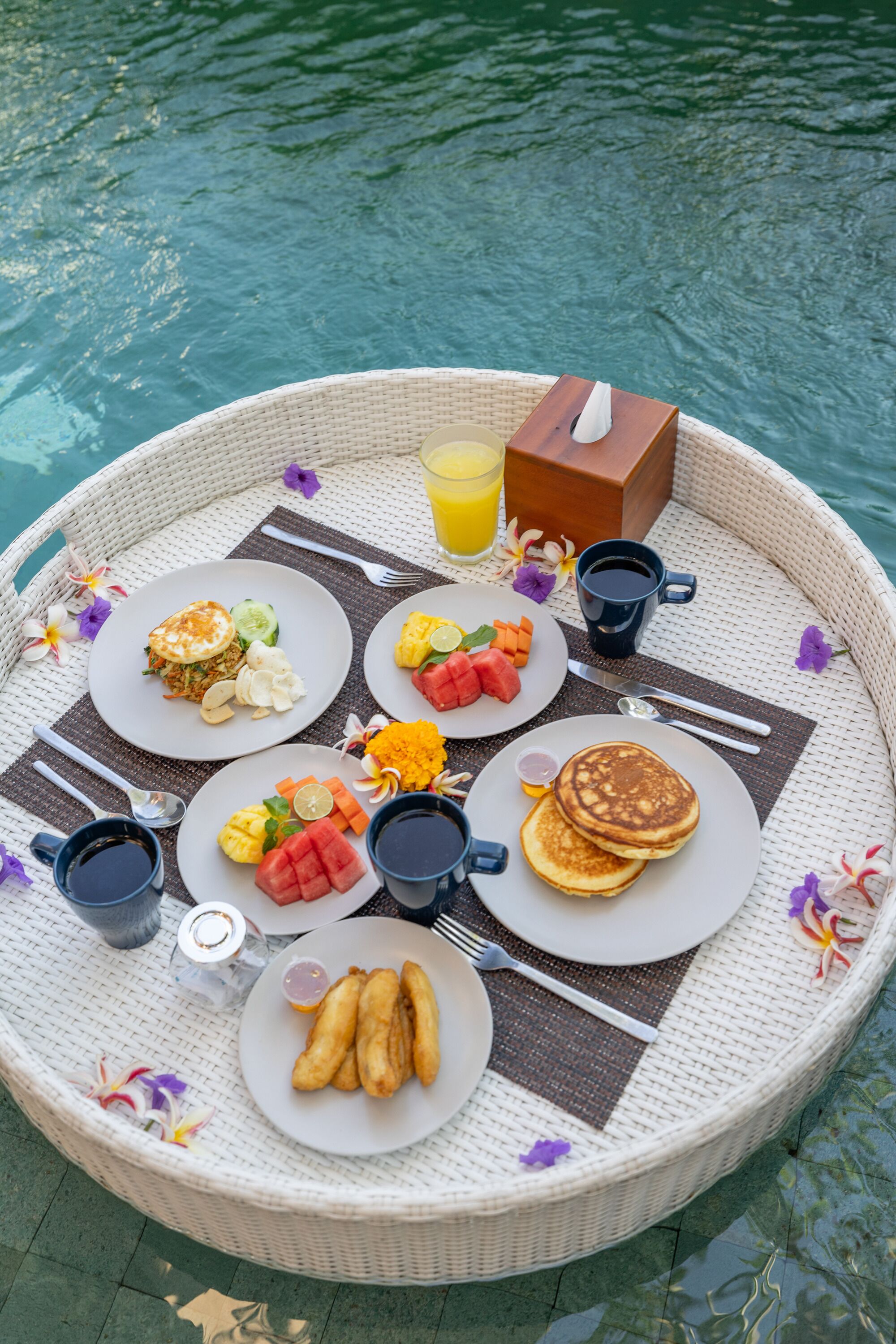 A breakfast tray with pancakes, fruit, and beverages by a pool.