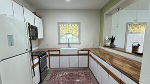Une cuisine avec des meubles blancs, un plan de travail en bois, un tapis à motifs et une fenêtre donnant sur un beau paysage.