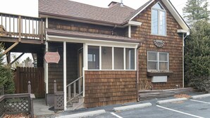 A two-story building with a brown shingle exterior, a visible entrance with a wooden door, and a sign indicating a suite. - Small Private suite with Electric Fireplace and Pet Friendly (Blowing Rock)
