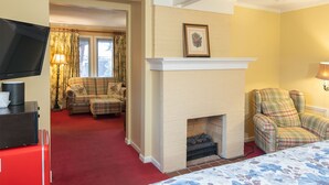 A room with a fireplace, two plaid armchairs, a television, and a bed with a floral bedspread. - Small Private suite with Electric Fireplace and Pet Friendly (Blowing Rock)