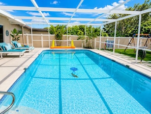 Une piscine d’un bleu éclatant, surmontée d’une pergola blanche, et entourée d’une clôture et de verdure.