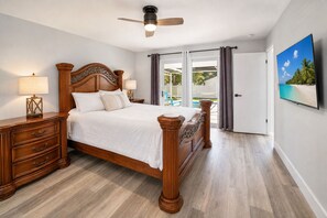 A bedroom with a wooden bed, a nightstand, a ceiling fan, and a view of a pool through a glass door.