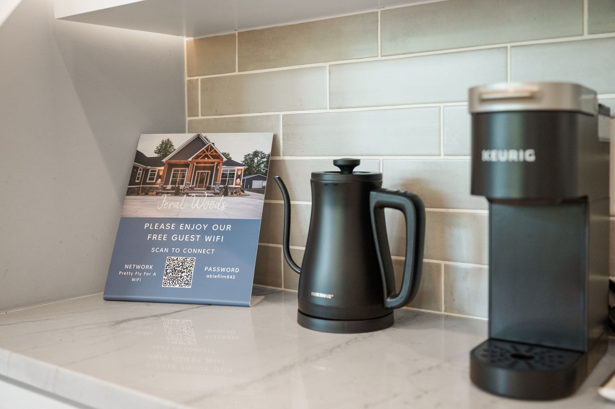 A coffee maker, a sign offering free guest WiFi, and a QR code on a kitchen counter.