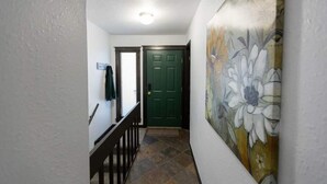 Um corredor com porta verde, escada e painel floral na parede.