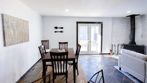 Uma área de refeições com mesa e cadeiras, um sofá, uma lareira e uma porta que dá para o exterior.