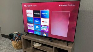 Uma TV TCL Roku sobre um suporte de madeira, com um controle remoto em cima.