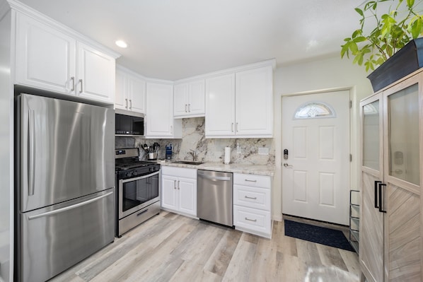 A modern kitchen with white cabinets, stainless steel appliances, and a marble backsplash.