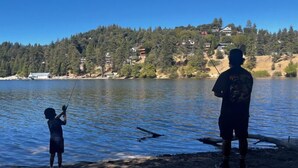 A lake with two people fishing, surrounded by a forested hillside with houses.