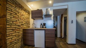 Een compacte keuken met een bakstenen muur, houten keukenkastjes, een inbouwkoelkast en een moderne kookplaat.