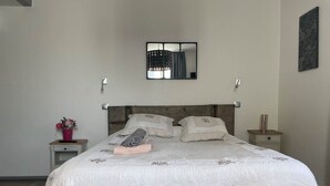 A neatly made bed with a quilted white bedspread, a wooden headboard, and a small bedside table with a vase of flowers. - GITE VAUBAN NEUF-BRISACH (NEUF BRISACH)