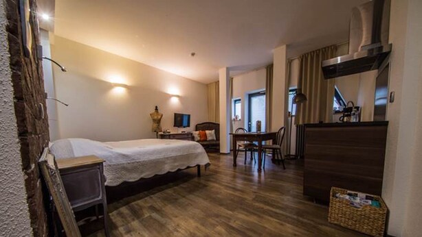 A hotel room with a bed, a desk, a chair, a television, and a kitchenette area.