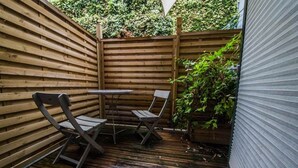 A wooden deck with a table and two chairs, surrounded by a wooden fence and greenery.