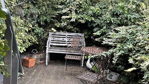 A wooden deck with a metal bench and a metal table, surrounded by dense foliage. - Saint Martin Guesthouse LE Vauban (NEUF BRISACH)