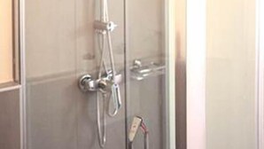 Een douchecabine met glazen wanden, een handdouche en een muurbevestigde kraan.