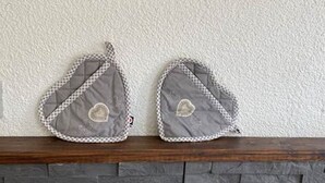 Two gray quilted oven mitts with heart patches on a wooden mantel above a stone fireplace. - Camaret Guesthouse LE Vauban (NEUF BRISACH)