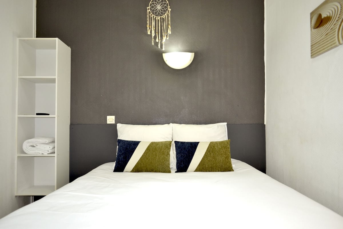 A neatly made bed with two pillows, a white wardrobe, and a wall-mounted light fixture.