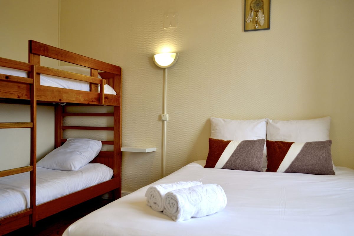 A room with a bunk bed, a single bed, and a wall-mounted light fixture.
