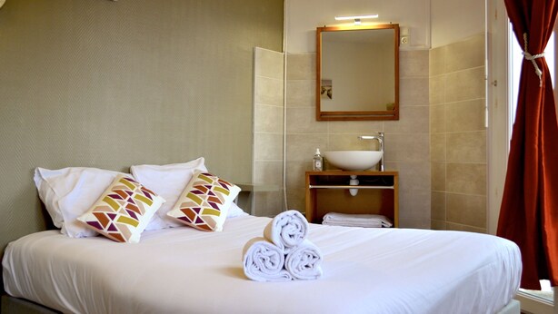 Une chambre d’hôtel avec un lit bien fait, une salle de bain avec un lavabo et un miroir, et une fenêtre avec des rideaux.