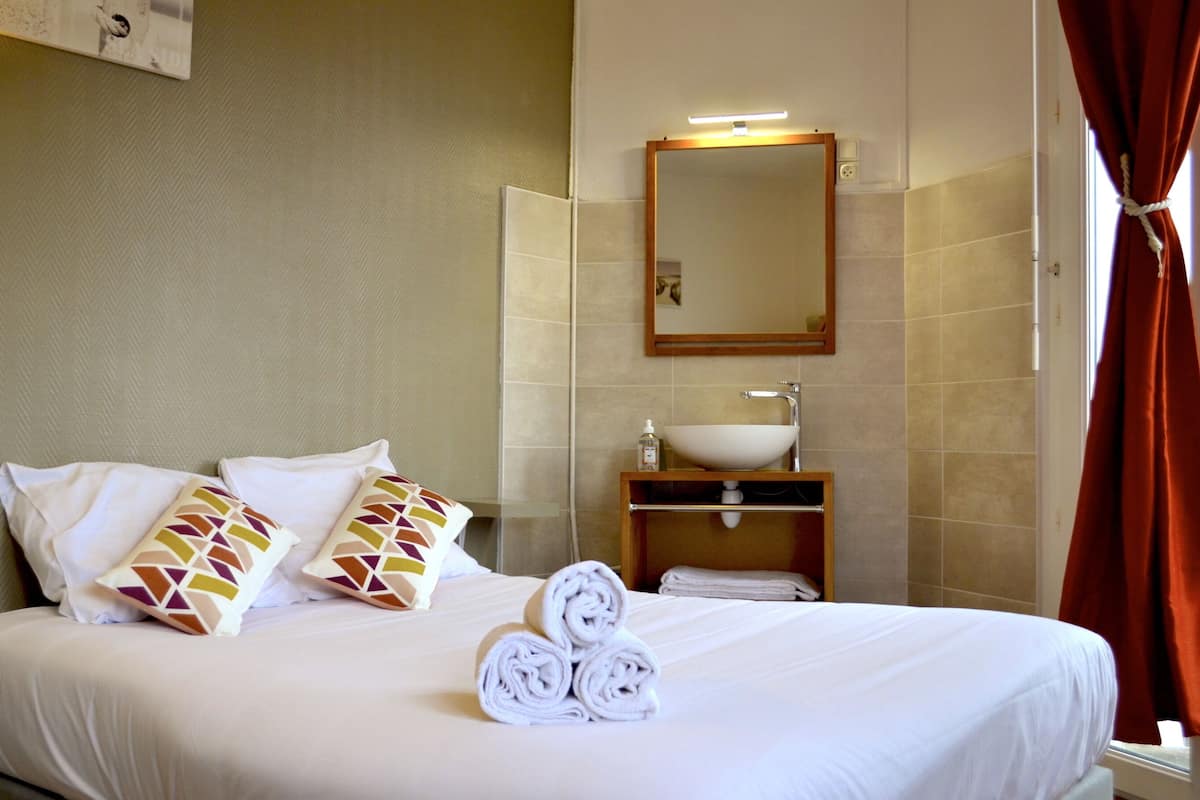 A hotel room with a neatly made bed, a bathroom with a sink and mirror, and a window with curtains.