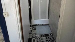 Une salle de bain avec un espace douche fermé, des carreaux de sol à motifs et une porte dotée d’une poignée.