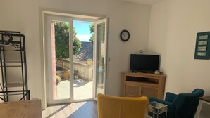 Una sala de estar con puerta de vidrio corrediza que da a un patio, un televisor sobre un mueble de madera y un sillón amarillo.