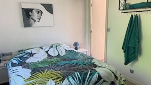 Un dormitorio con una cama, un estante con toallas, un cuadro y una puerta que da a otra habitación.