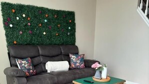 Ein Wohnzimmer mit grüner Wand, einem dunklen Sofa, floralen Kissen, einem Holztisch und einem großen Teppich mit Blumenmuster.