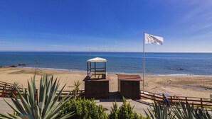 Vista a la playa con una bandera, una estructura cubierta y un edificio de madera.
