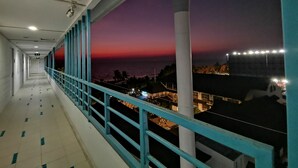 Un pasillo con barandilla, vista del atardecer y una ciudad lejana.