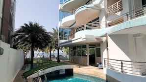 Un edificio moderno con piscina, mobiliario exterior y una palmera.