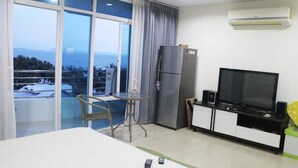 Habitación de hotel moderna con balcón, una mesa de comedor, refrigerador, televisión y un mueble bajo.