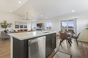 A modern kitchen with a central island, a dining area with a table and chairs, and a living space with a sofa and decorative items. - New, Stylish & centrally located. By Ford Idaho Center, shops & restaurants! (Nampa)