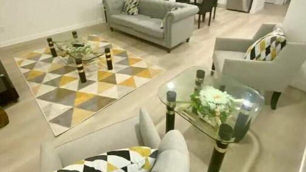 Ein modernes Wohnzimmer mit grauem Sofa, Glastisch und einem gemusterten Teppich.