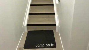 Eine Treppe mit einer schwarzen Matte am Fuß, auf der steht: 'Hereinkommen'.