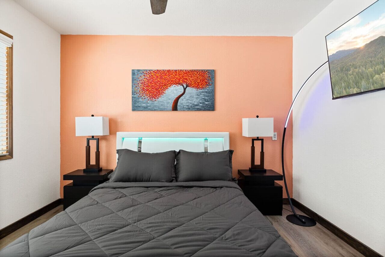 Ein Hotelzimmer mit einem Bett, zwei Nachttischen, einem Wandbild und einem an der Wand befestigten Fernseher.