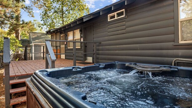 Un bain à remous se trouve devant une cabane en bois, qui est dotée d’une terrasse en bois et d’une rambarde en métal.