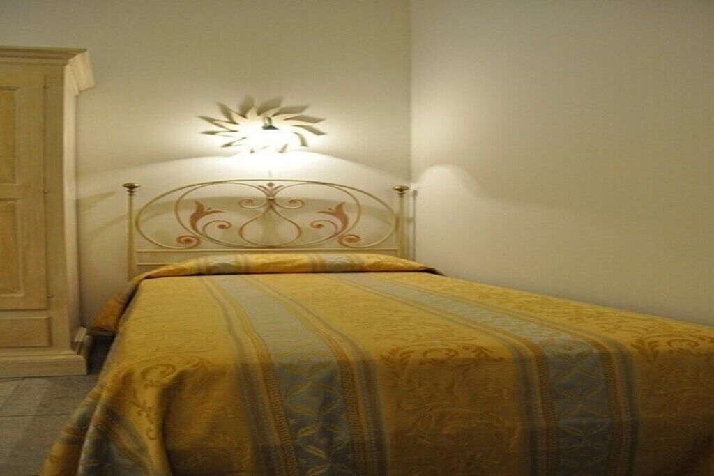 A single bed with a headboard and a bedside table, a wall-mounted light fixture, and a plain wall.