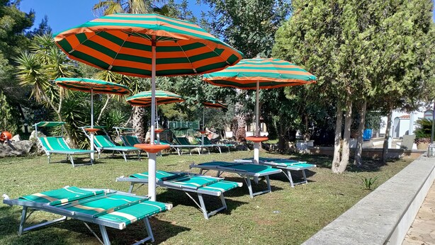 Un espace aménagé au bord de la piscine, avec plusieurs chaises longues et des parasols à rayures.